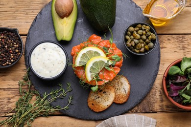 Photo of Delicious salmon tartare with avocado, sauce and croutons on wooden table, flat lay