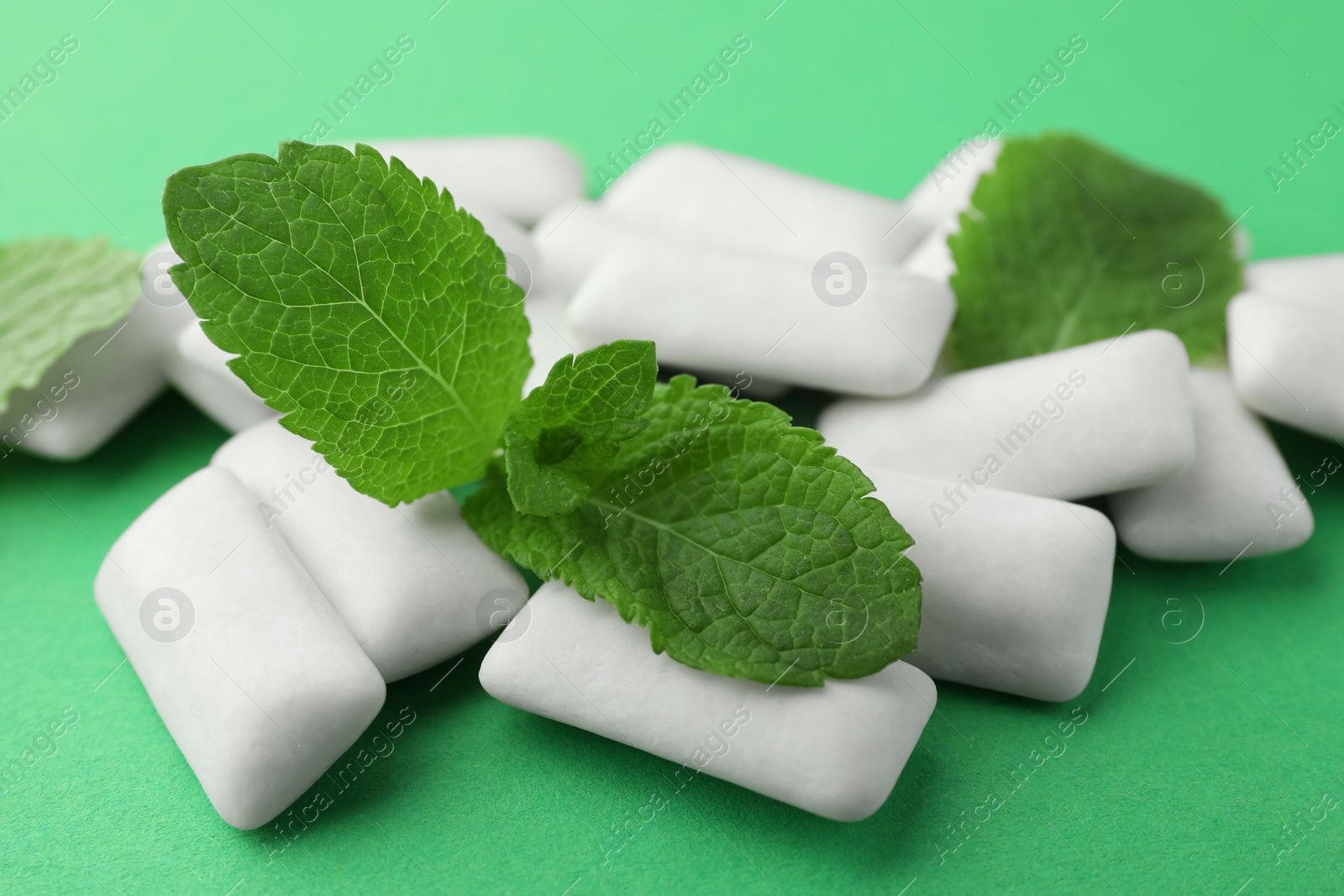 Photo of Tasty white chewing gums and mint leaves on green background, closeup