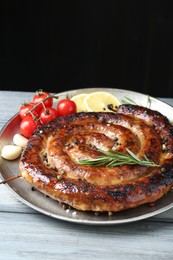 Delicious homemade sausage with spices, tomatoes and lemon on light grey wooden table against black background