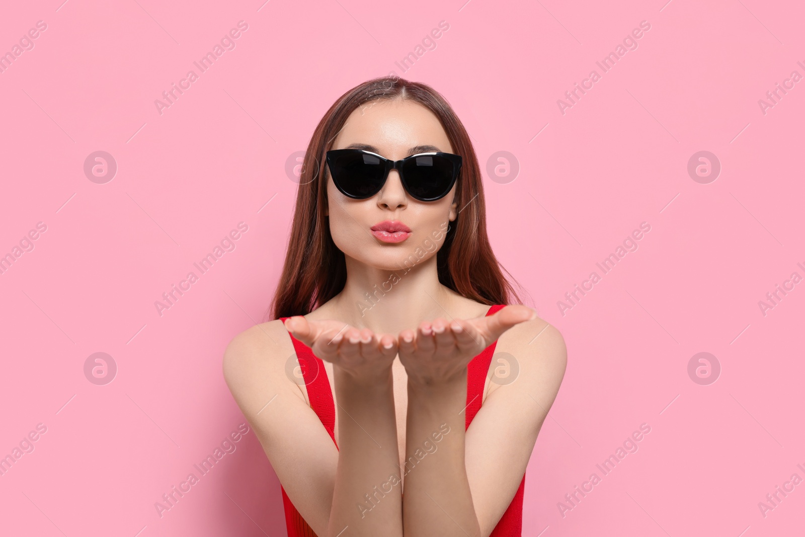 Photo of Beautiful young woman with sunglasses blowing kiss on pink background