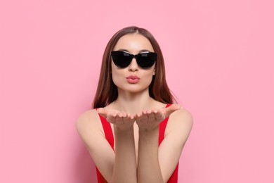 Photo of Beautiful young woman with sunglasses blowing kiss on pink background