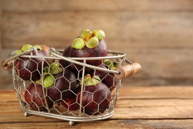 Photo of Fresh ripe mangosteen fruits in metal basket on wooden table. Space for text