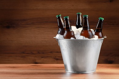 Photo of Metal bucket with bottles of beer and ice cubes on wooden table, space for text