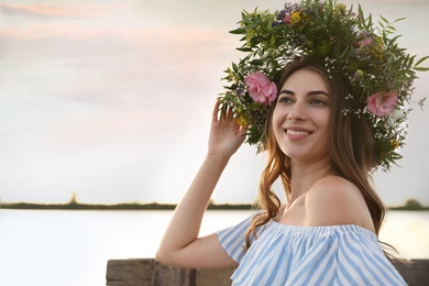 Photo of Young woman wearing wreath made of beautiful flowers near river