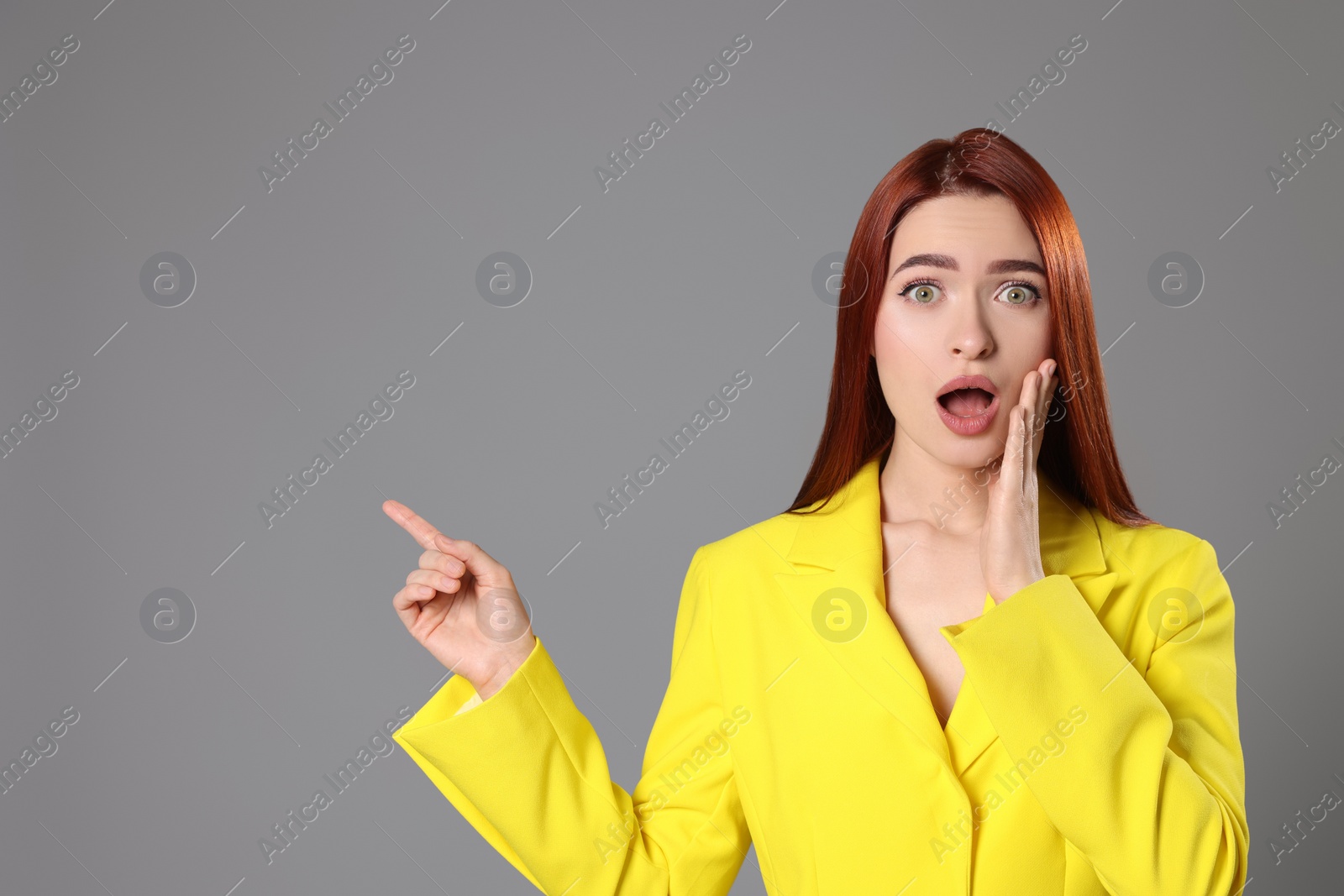 Photo of Confused woman with red dyed hair pointing somewhere on light gray background, space for text