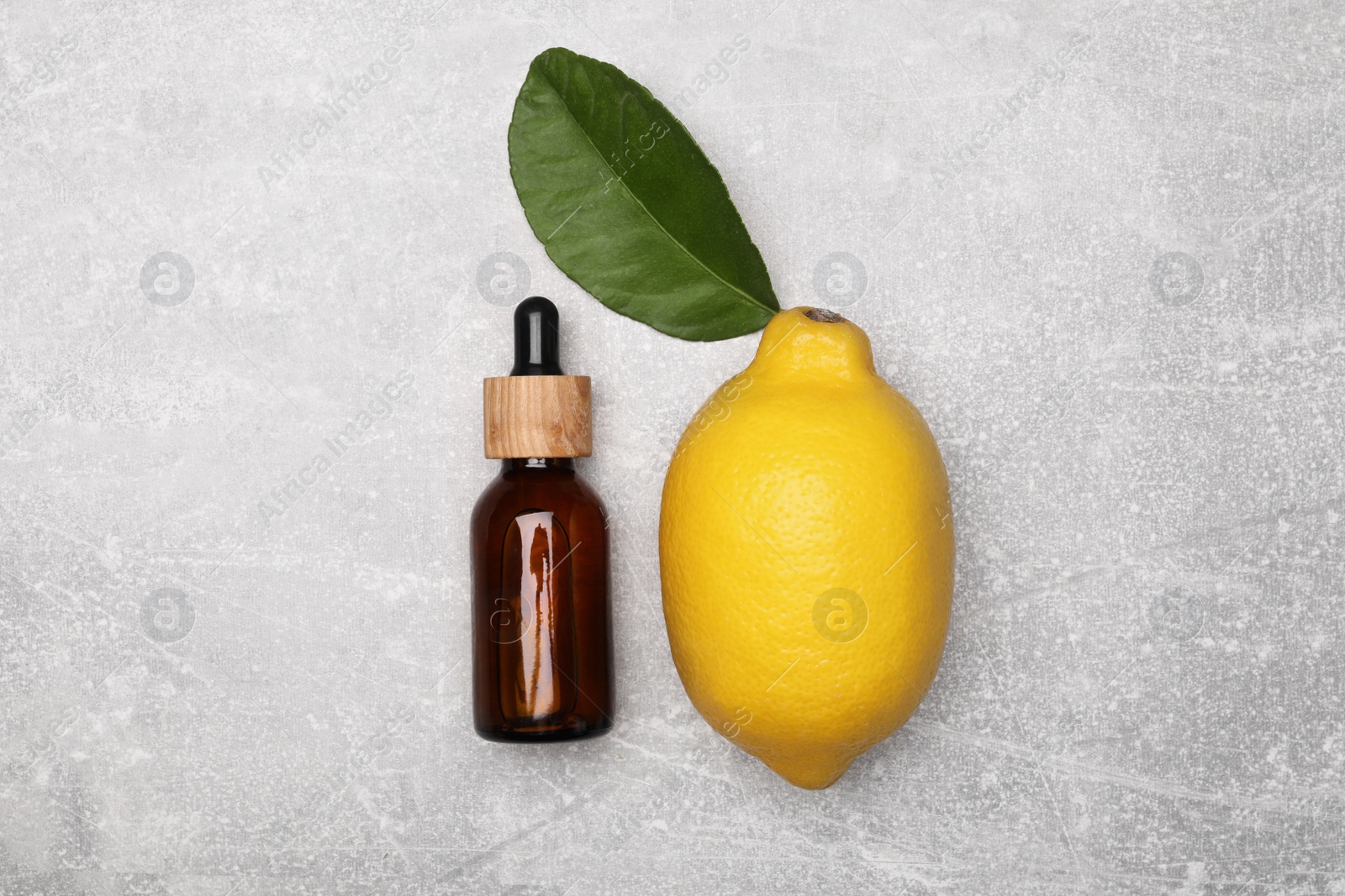 Photo of Bottle of essential oil with lemon and leaf on grey table, flat lay