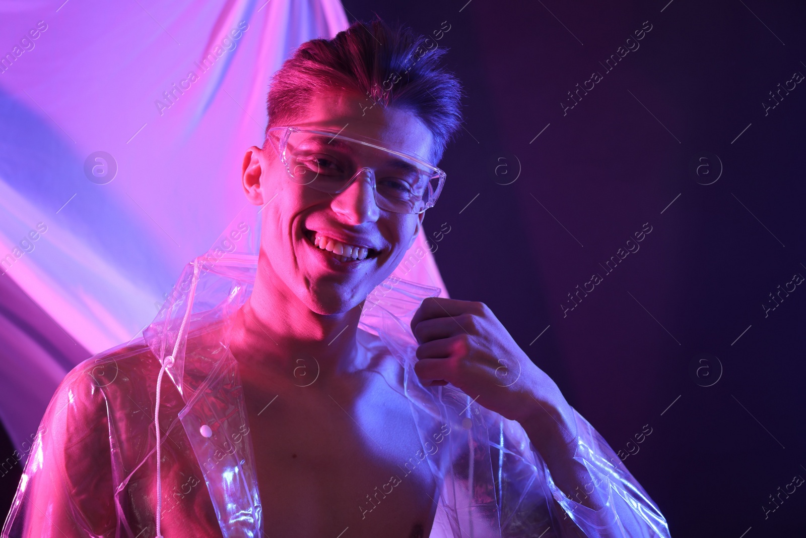 Photo of Stylish young man wearing clear coat and glasses in neon lights