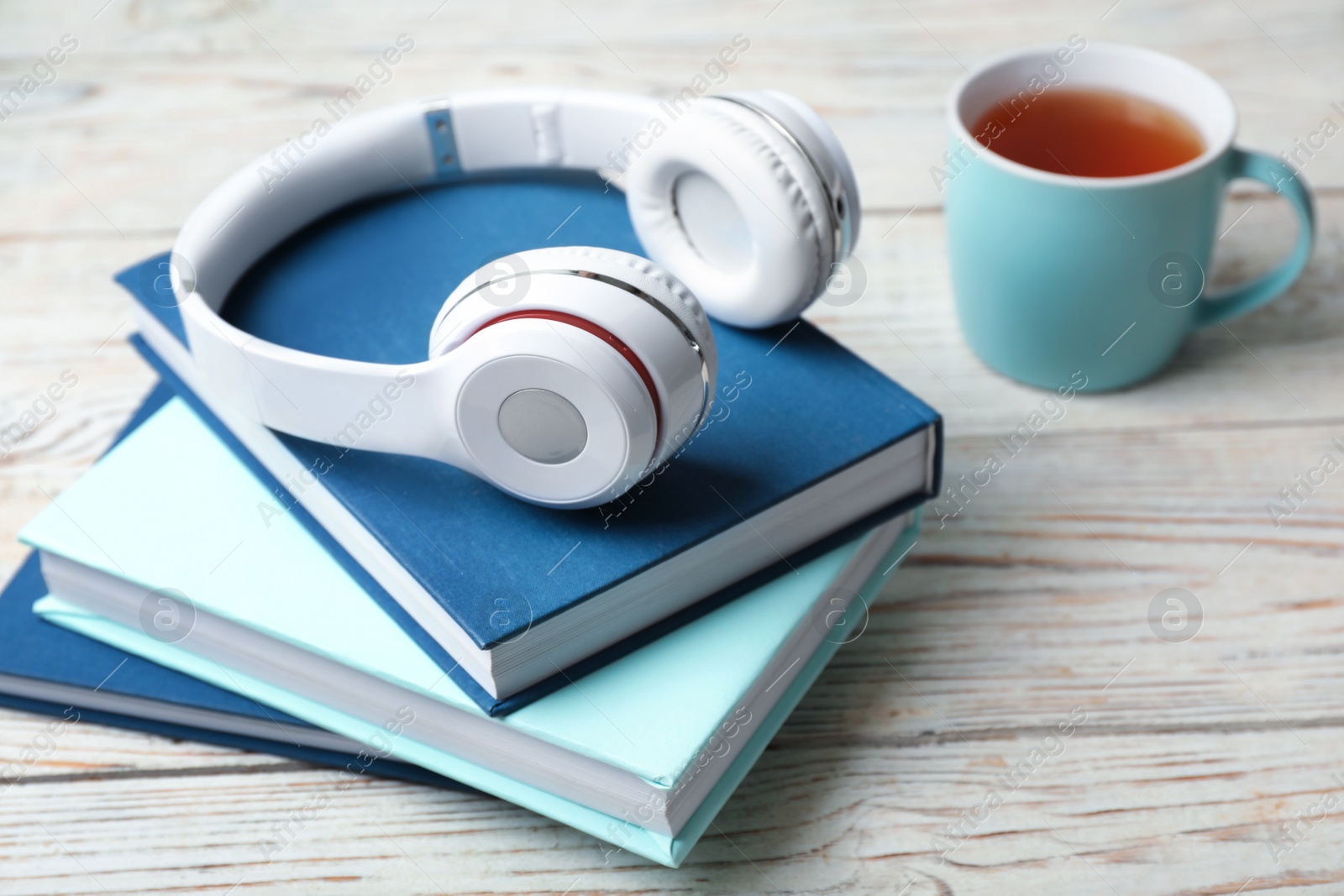 Photo of Modern headphones with hardcover books on wooden table