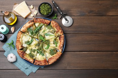 Photo of Delicious pizza with pesto, cheese and arugula served on wooden table, flat lay. Space for text