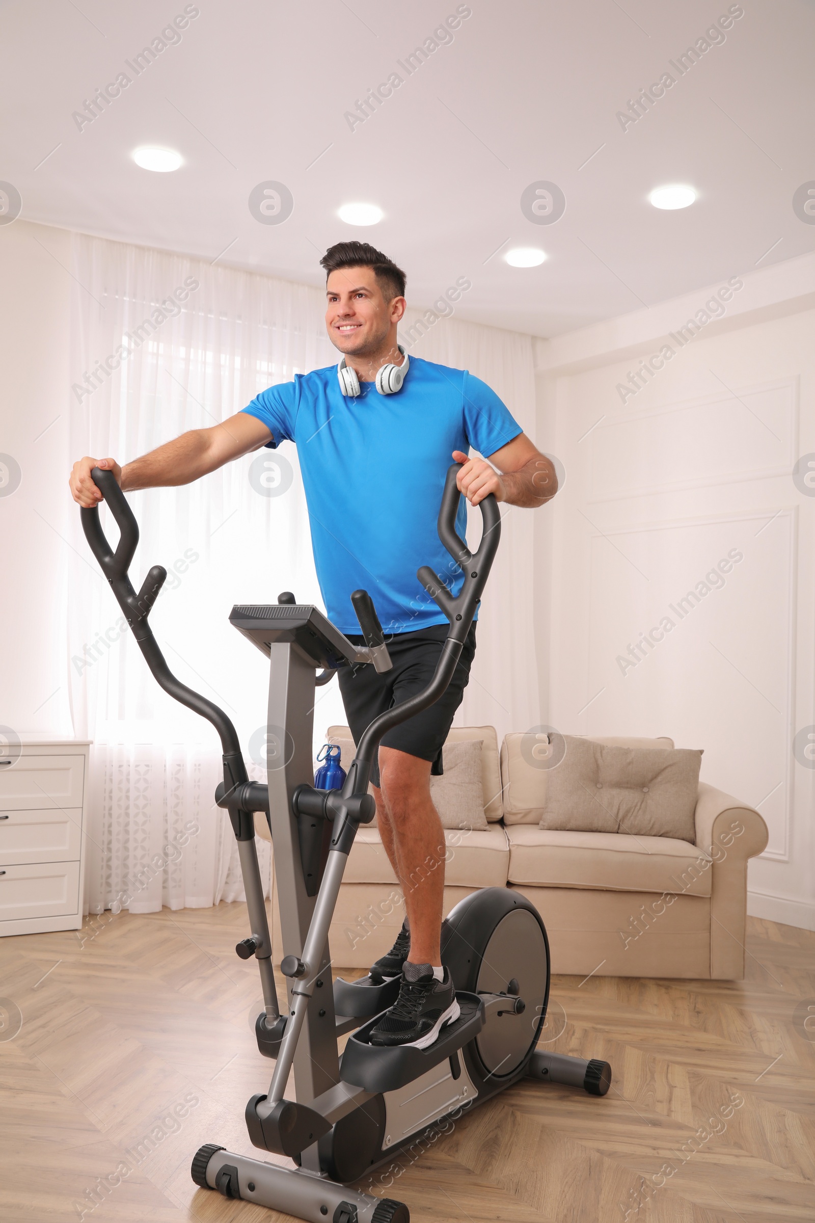 Photo of Man with headphones using modern elliptical machine at home