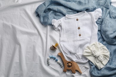 Flat lay composition with cute baby clothes and accessories on white bedsheet, space for text