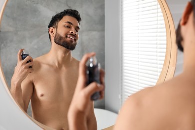 Photo of Man spraying luxury perfume near mirror indoors