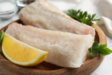 Photo of Fresh raw cod fillets with parsley and lemon on white table, closeup