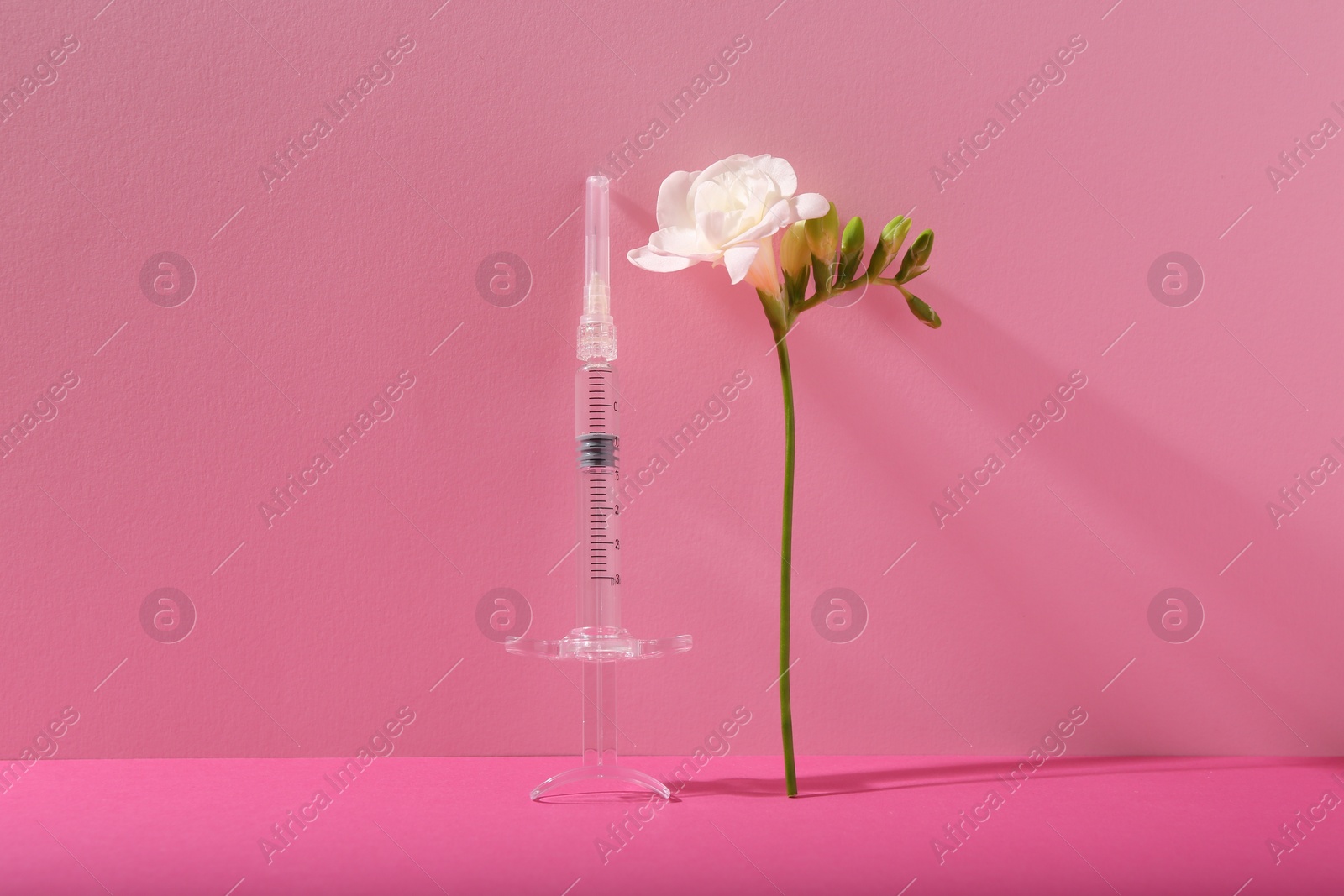 Photo of Cosmetology. Medical syringe and freesia flower on pink background