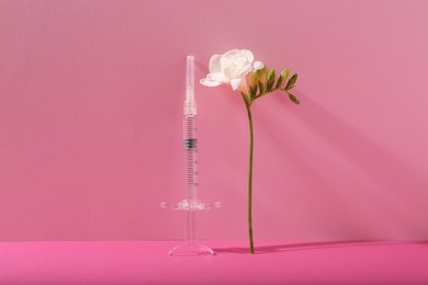 Cosmetology. Medical syringe and freesia flower on pink background