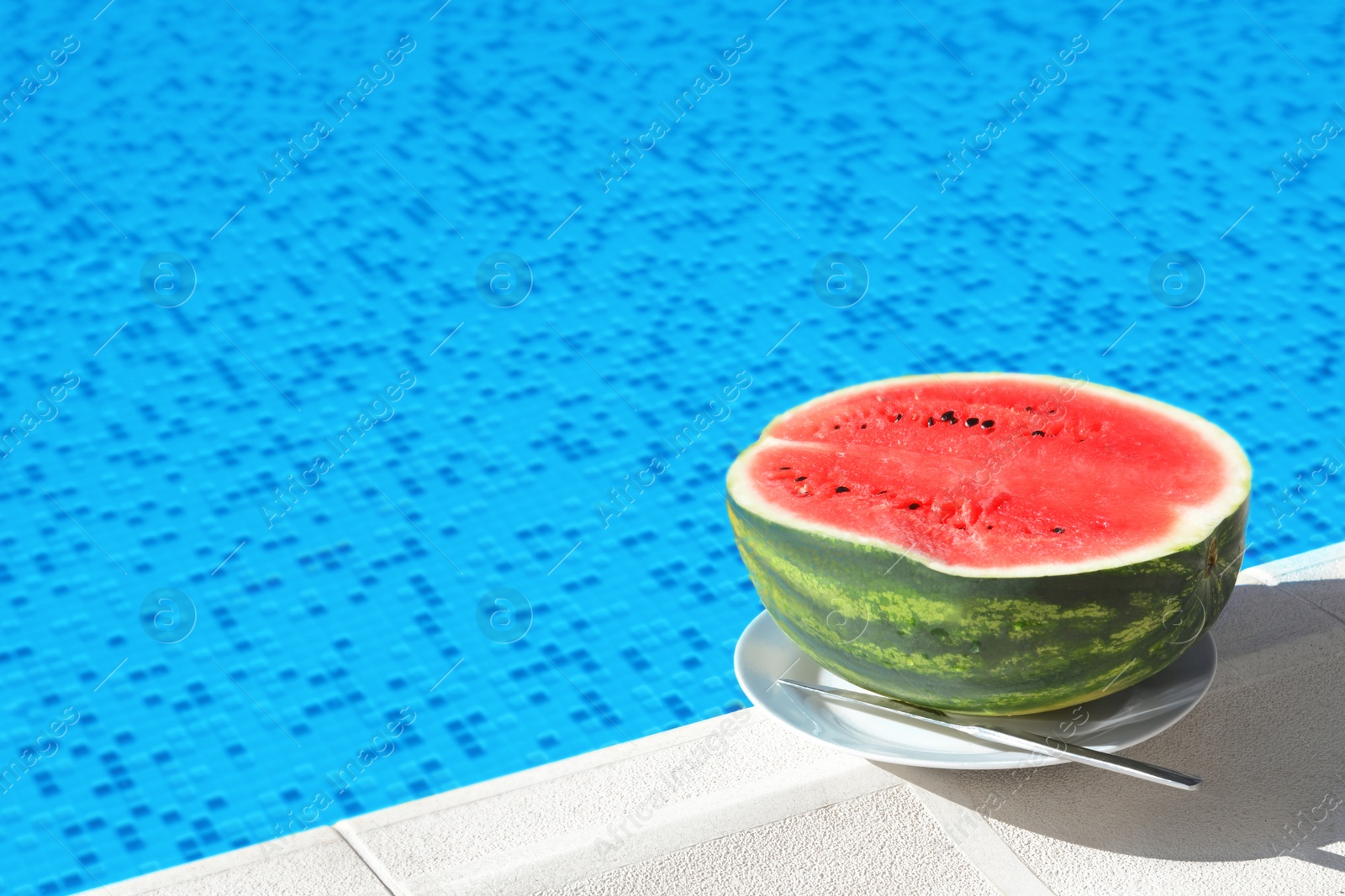 Photo of Half of fresh juicy watermelon on plate near swimming pool outdoors. Space for text