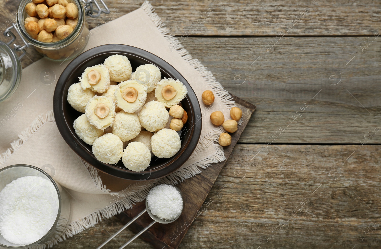 Photo of Delicious candies with coconut flakes, hazelnut and ingredients on wooden table, flat lay. Space for text