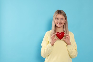 Photo of Happy volunteer holding red heart with hands on light blue background. Space for text