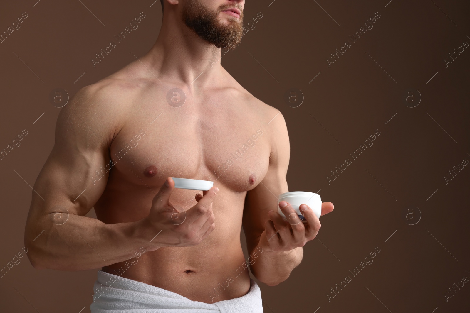 Photo of Handsome man holding jar with moisturizing cream on brown background, closeup. Space for text