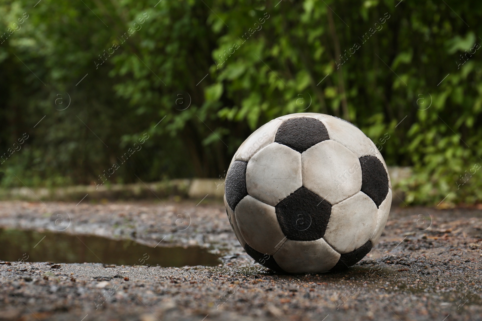 Photo of Dirty soccer ball near puddle on ground, space for text