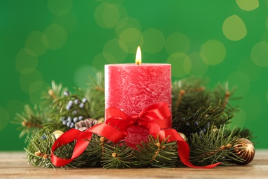 Photo of Burning red candle and Christmas decor on table against green background with bokeh effect