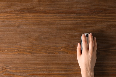 Woman using computer mouse on wooden background, top view. Space for text