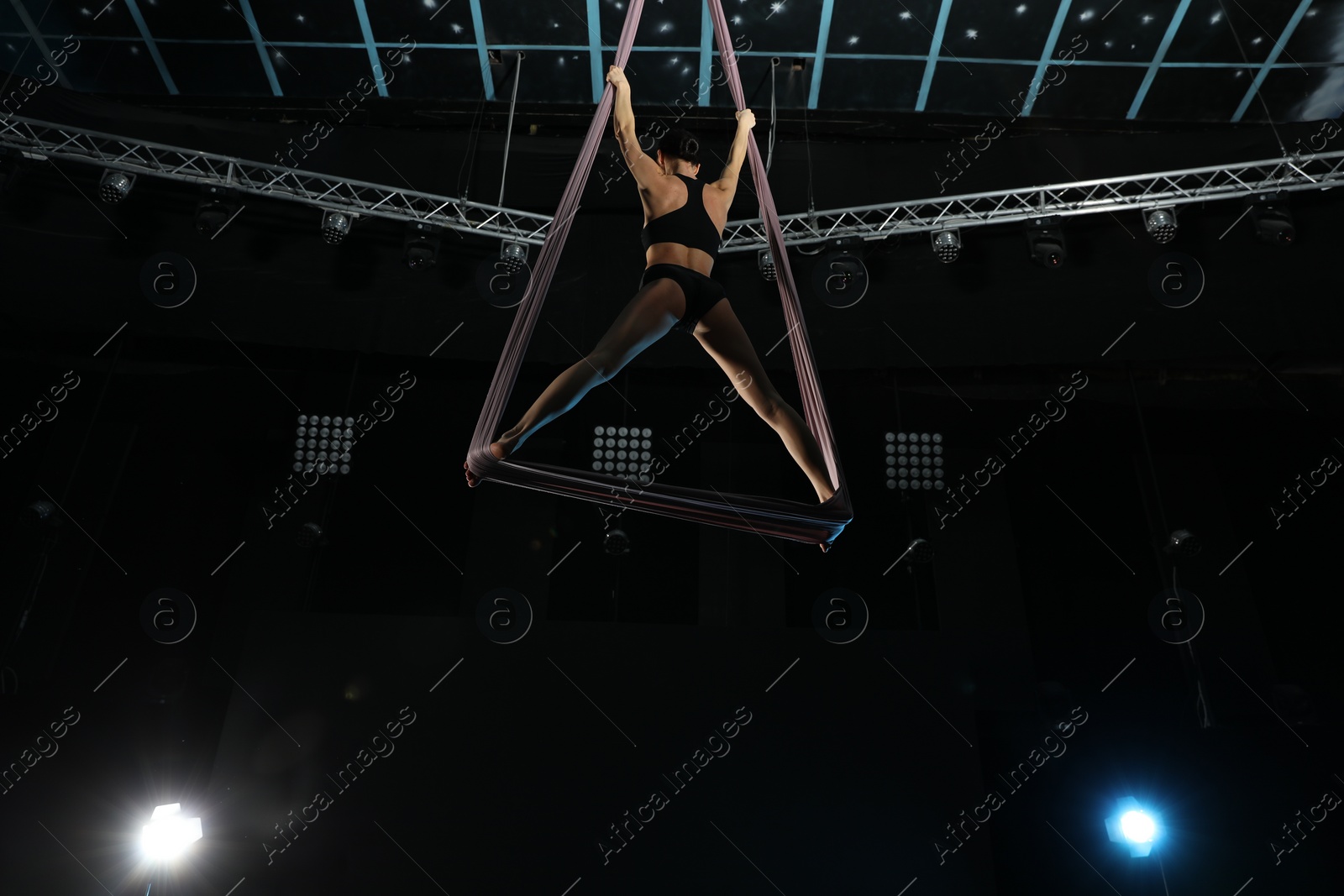 Photo of Young woman performing acrobatic element on aerial silk indoors