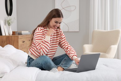 Happy woman with laptop on bed in bedroom