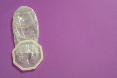 Photo of Unrolled female condom on violet background, top view and space for text. Safe sex