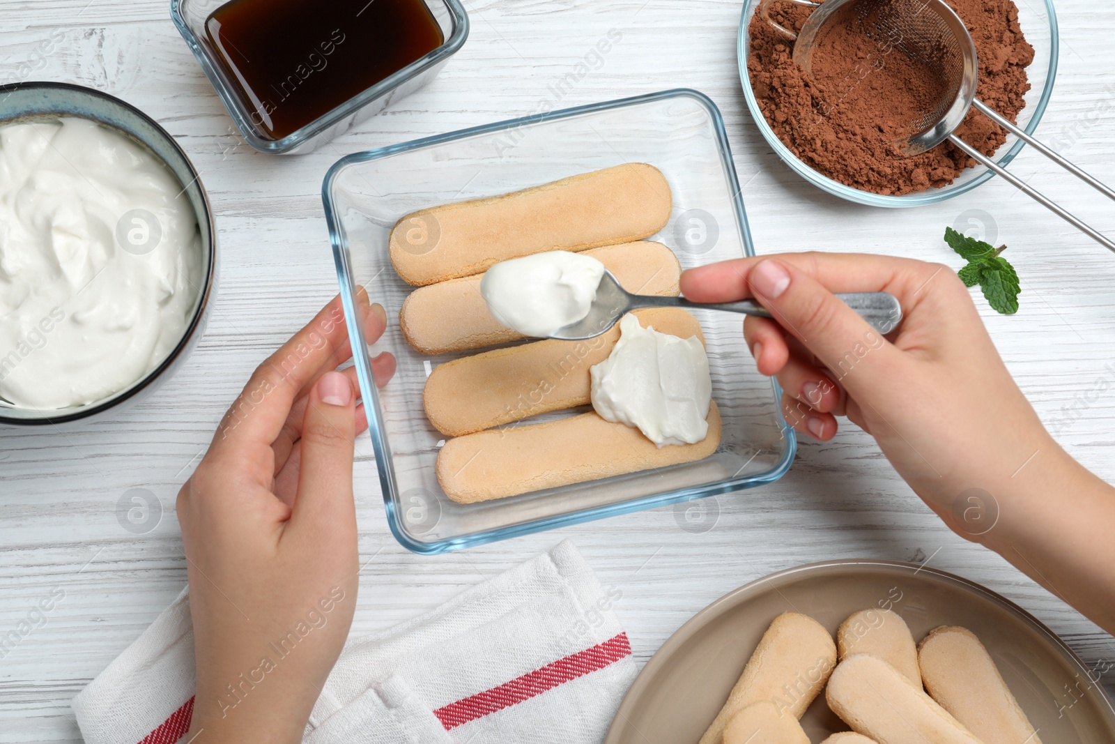 Photo of Woman making tiramisu cake at white wooden table, top view