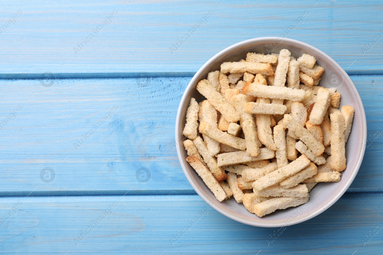 Photo of Crispy wheat rusks in bowl on light blue wooden table, top view. Space for text