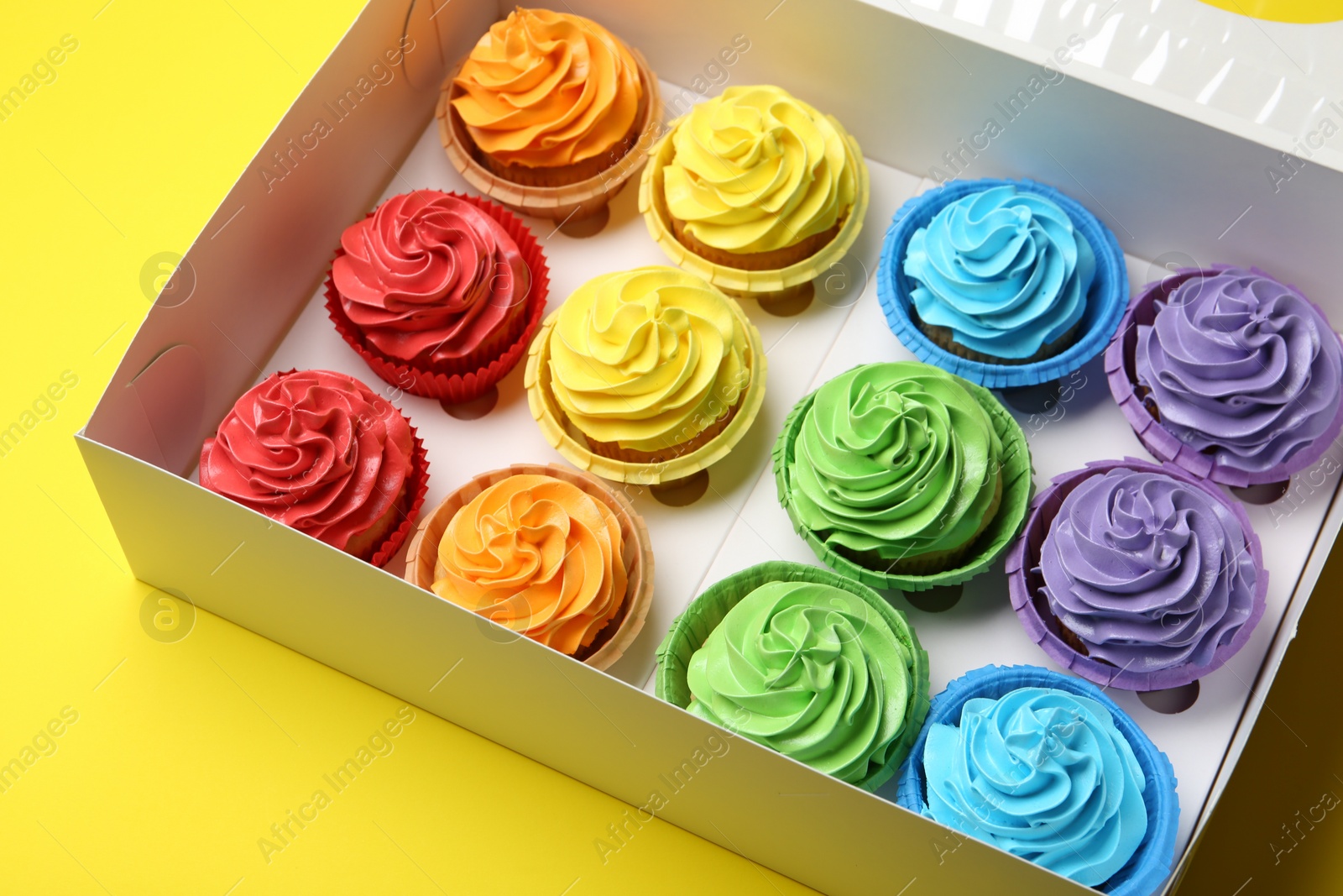 Photo of Tasty cupcakes in box on yellow background, closeup