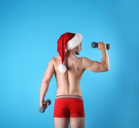 Photo of Shirtless sexy young Santa Claus with dumbbells on color background