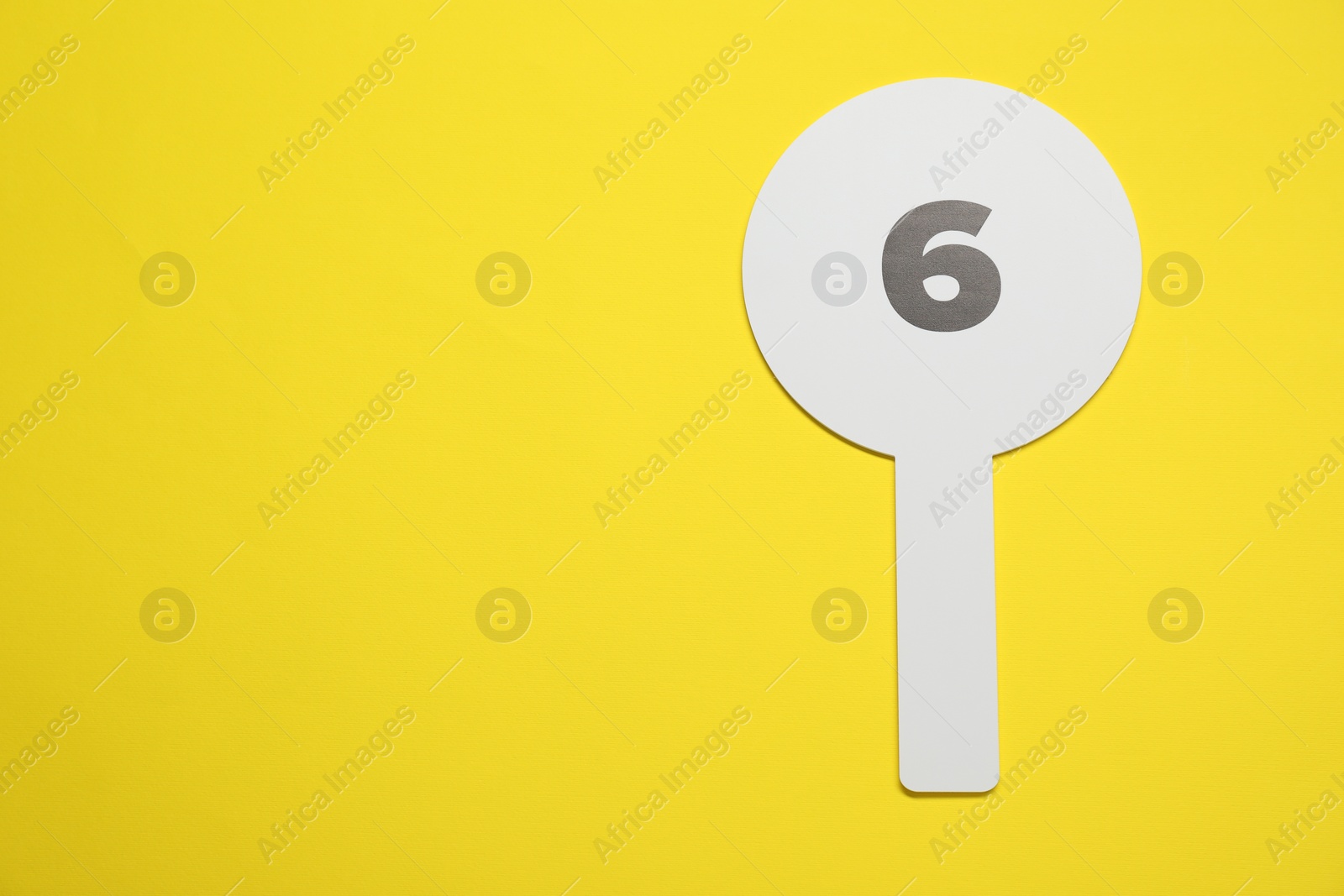 Photo of Auction paddle with number 6 on yellow background, top view. Space for text