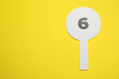 Photo of Auction paddle with number 6 on yellow background, top view. Space for text