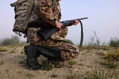 Man wearing camouflage with hunting rifle and backpack outdoors, closeup