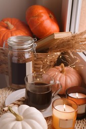 Photo of Cup of hot drink, jar with coffee beans, candles and pumpkins on window sill indoors