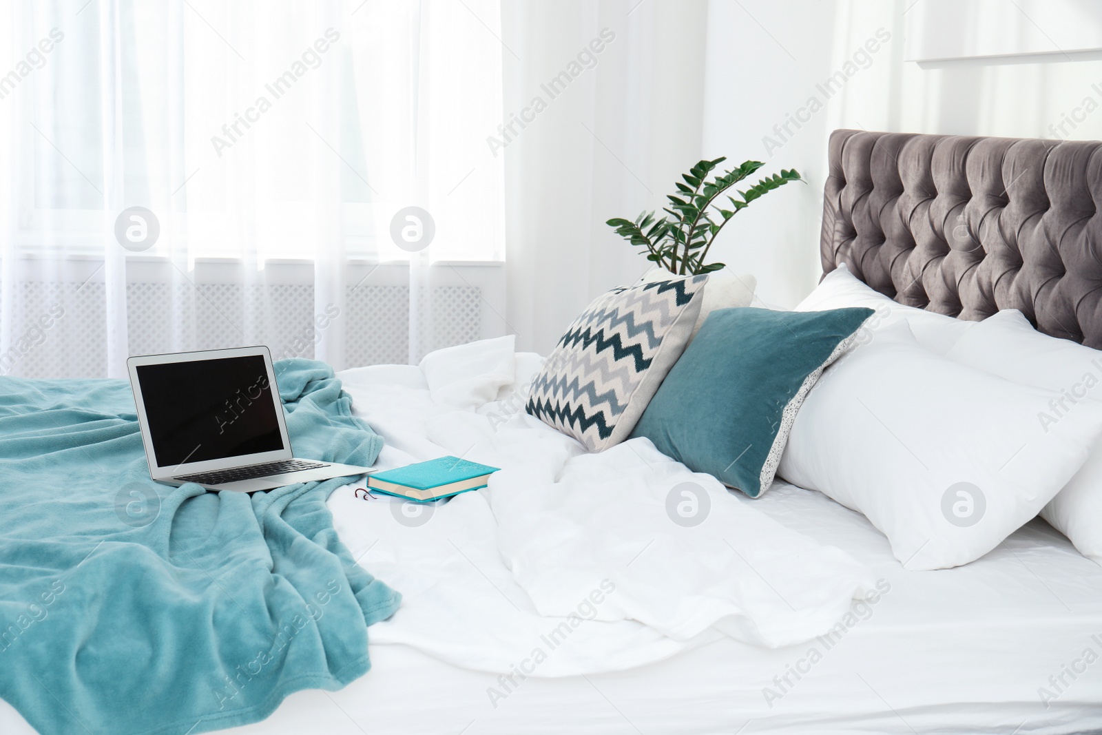 Photo of Laptop and books on bed in stylish room interior. Space for text