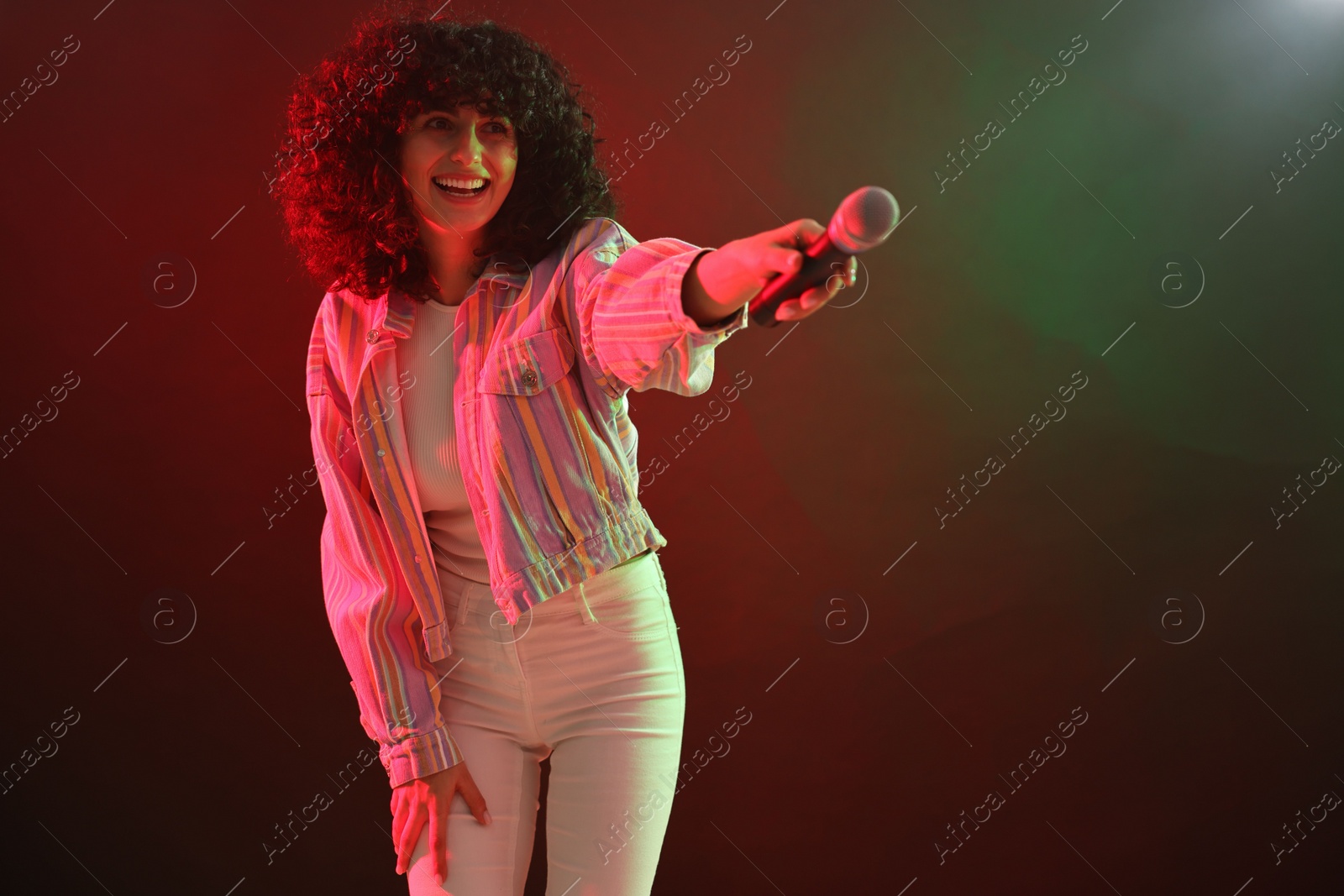 Photo of Beautiful young woman with microphone on color background in neon lights