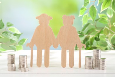 Photo of Pension savings. Figure of senior couple and stacked coins on white wooden table outdoors