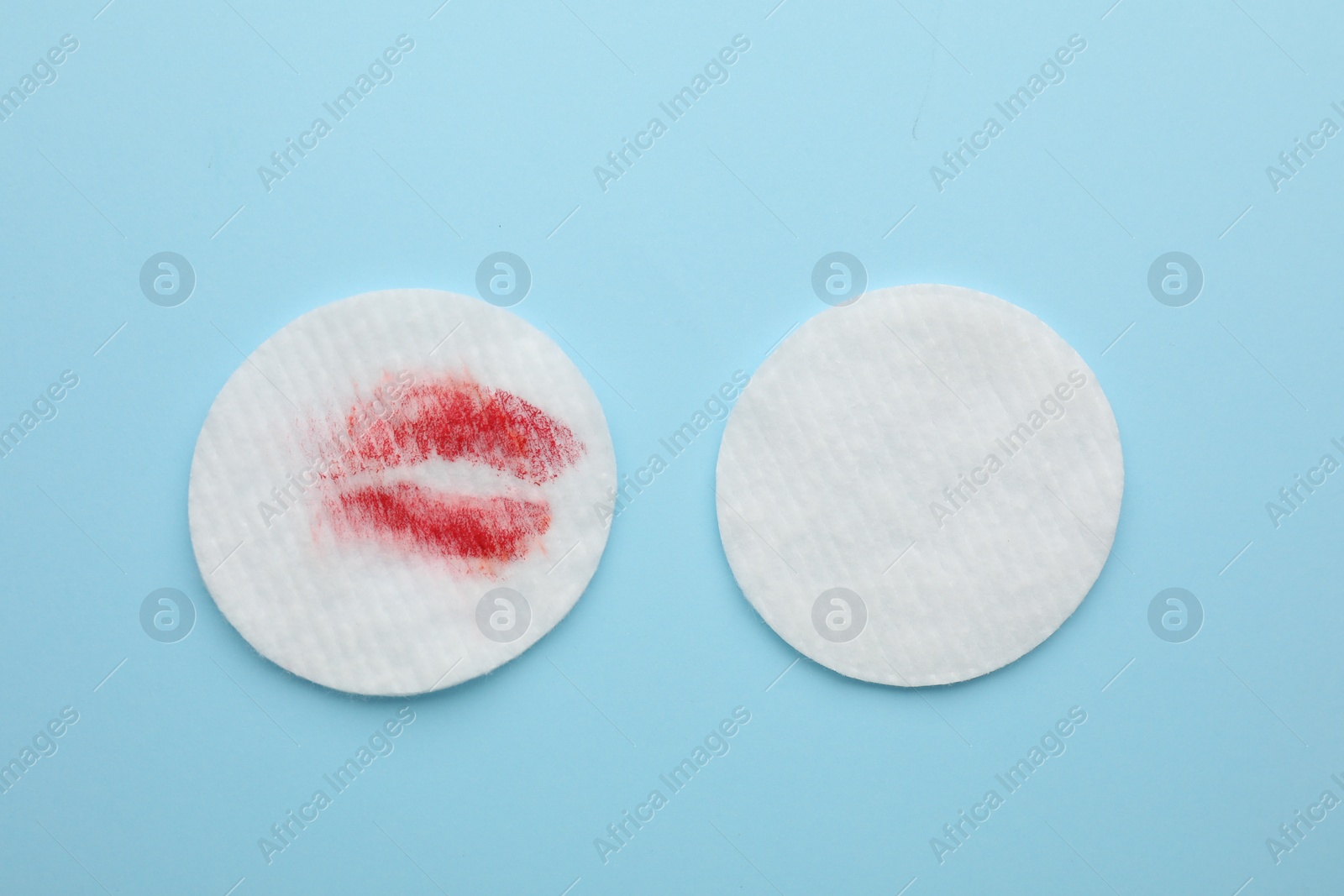 Photo of Clean and dirty cotton pads after removing makeup on light blue background, flat lay