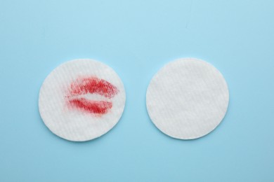 Photo of Clean and dirty cotton pads after removing makeup on light blue background, flat lay