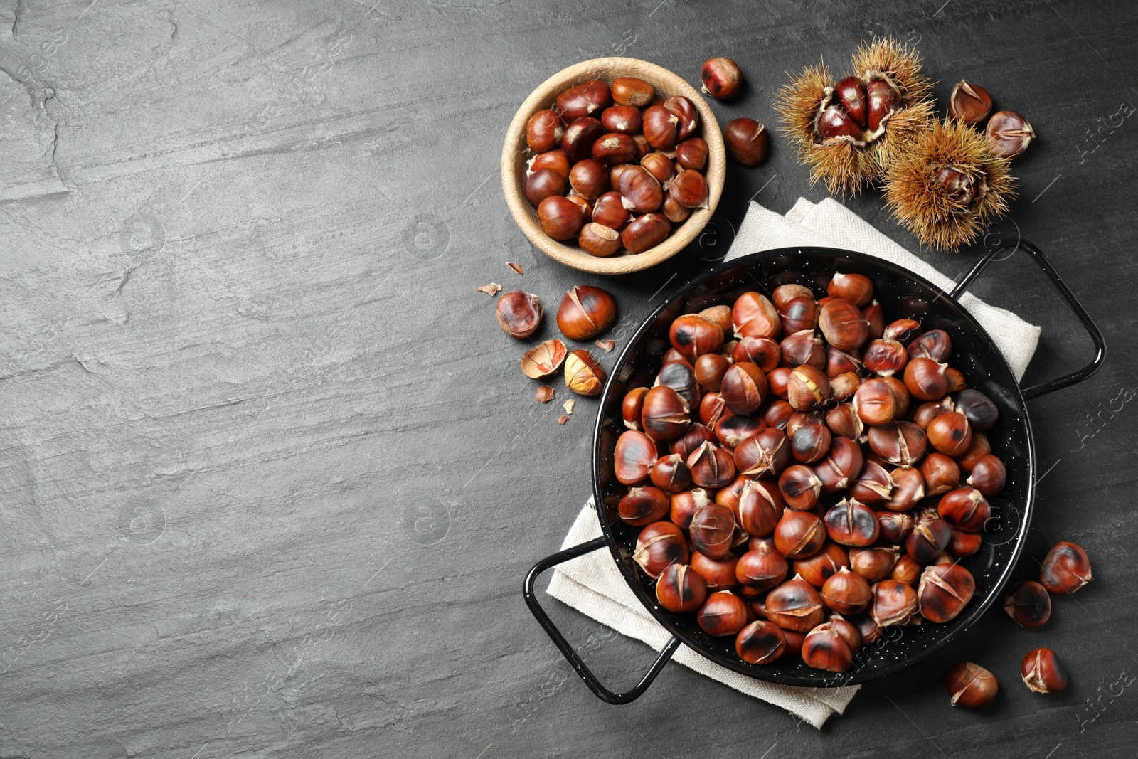 Photo of Delicious roasted edible chestnuts on black slate table, flat lay. Space for text