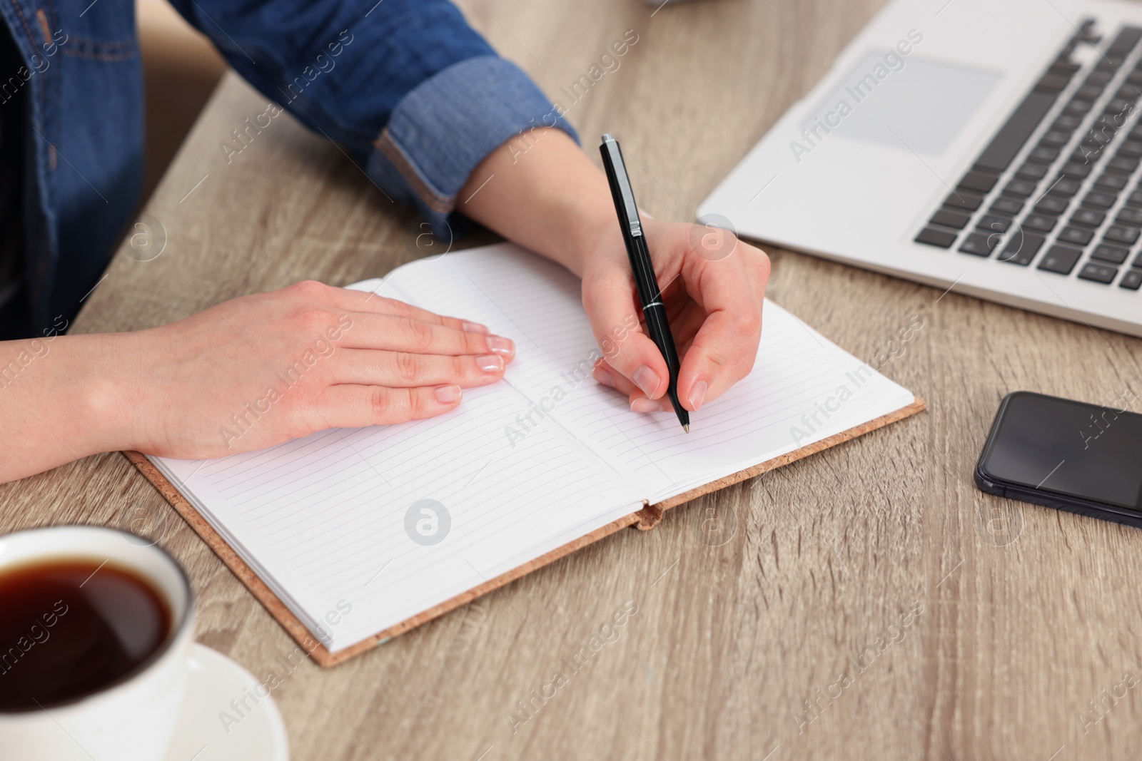 Photo of Young woman writing in notebook at wooden table, closeup