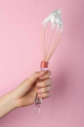 Woman holding whisk with whipped cream on pink background, closeup