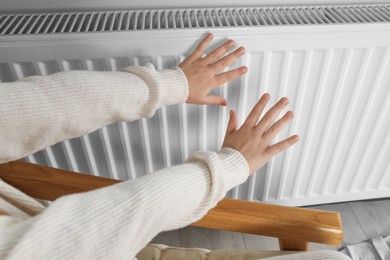 Photo of Little girl warming hands near heating radiator indoors, closeup