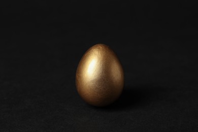 One shiny golden egg on black background