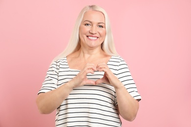 Photo of Mature woman making heart with her hands on color background