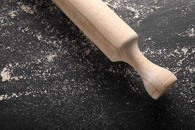 Photo of Scattered flour and rolling pin on dark textured table, top view