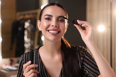 Bright makeup. Beautiful woman applying mascara in dressing room